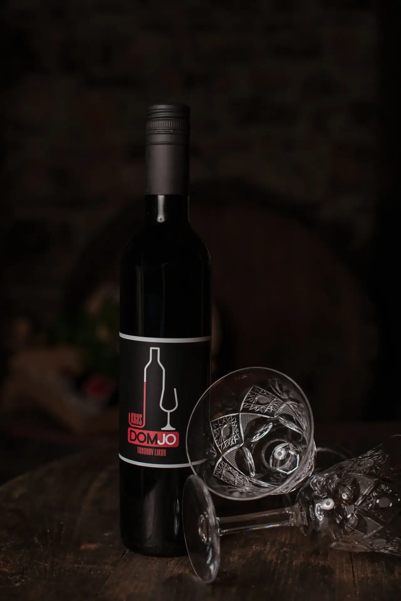 Elegantna temna produktna fotografija steklenice vina DOMJO ob kristalnem kozarcu.