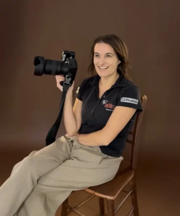 fotografinja-vani-portret-o-meni Nasmejana profesionalna fotografinja Vani sedi v svojem studiu s fotoaparatom v roki.