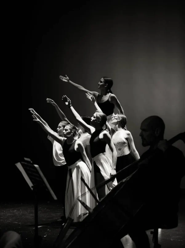 Črno-bela fotografija plesalcev z dvignjenimi rokami med umetniškim nastopom na koncertu Inmusic.