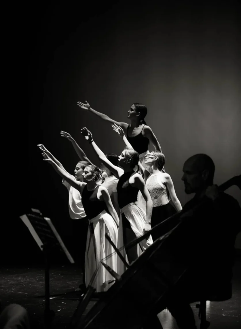 Črno-bela fotografija plesalcev z dvignjenimi rokami med umetniškim nastopom na koncertu Inmusic.