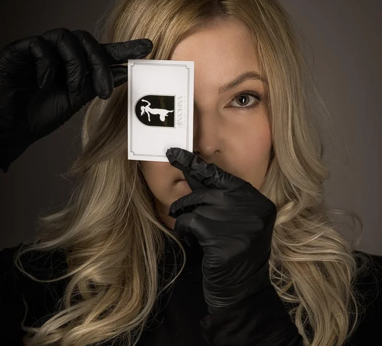 Skrivnosten in eleganten komercialni portret ženske, ki ima eno oko pokrito z roko in gostimi umetnimi trepalnicami, branded 'Sinjorina'.