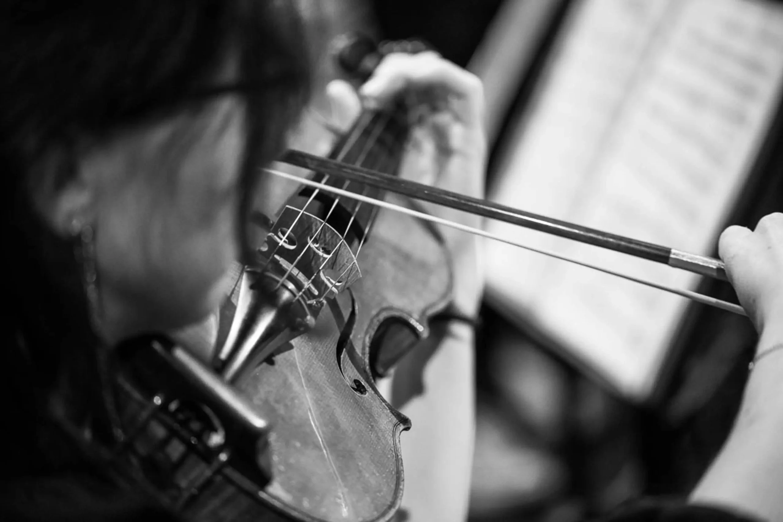 Detajl glasbenice med igranjem violine na koncertnem odru.