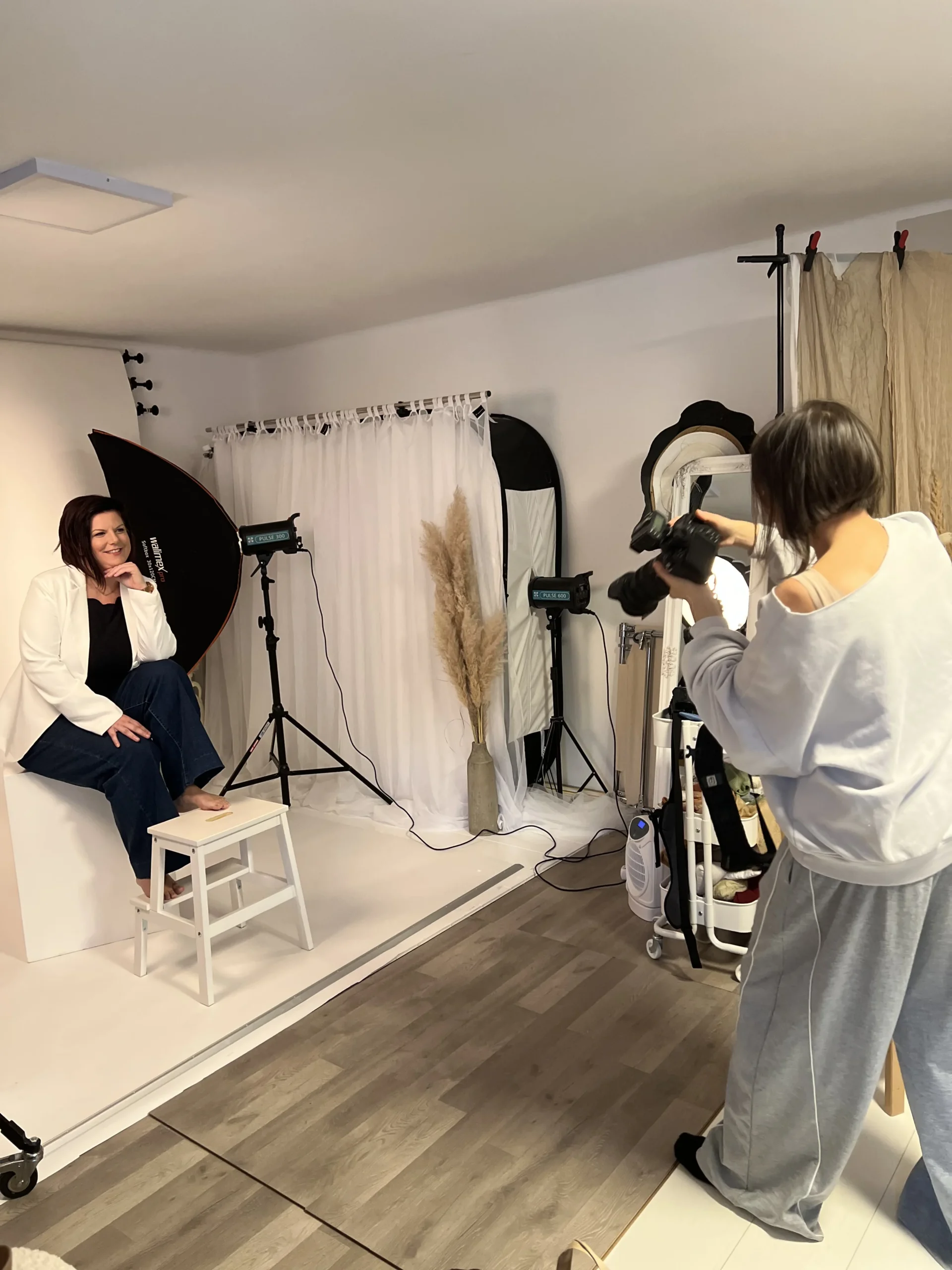 Fotografinja Vani fotografira žensko v svetlem studijskem ambientu z naravno dekoracijo.